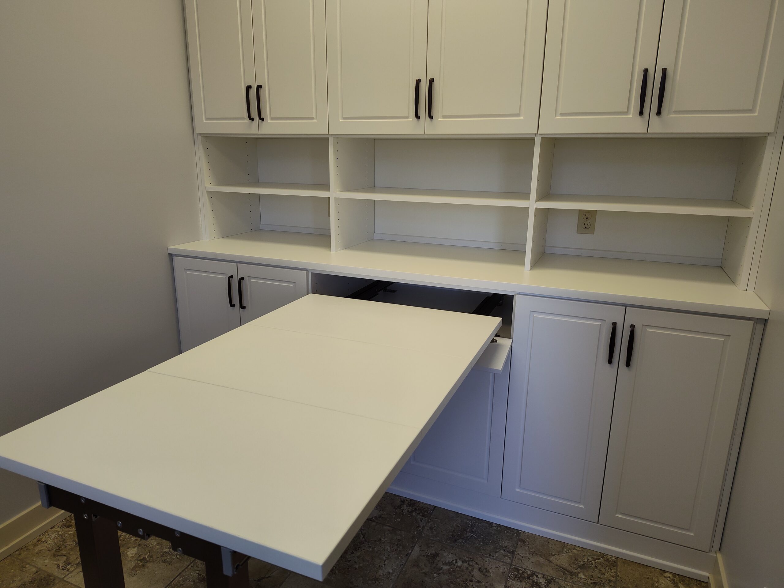A white built-in cabinet with open shelves and a pull-out table extended from the lower section, perfect for organizing careers materials in a room with tiled flooring.