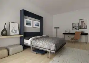 Modern bedroom with a Murphy bed pulled down, a desk and chair in the corner, wall art, and neutral-toned decor on a light wood floor, plus reach-in closet storage for added organization. Closet Concepts of Grand Rapids