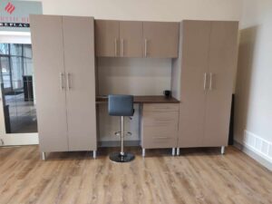 A modern office setup with taupe cabinets, a built-in desk, closet storage, a grey swivel chair, and a black mug on the wooden floor. Closet Concepts of Grand Rapids