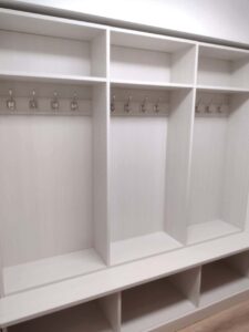 White built-in locker unit with three open sections, each containing metal hooks, a bench below, and cubby storage compartments at the top and bottom—an organized addition to any reach in closet. Closet Concepts of Grand Rapids