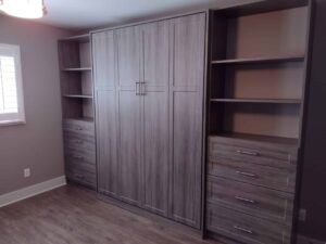 Built-in wooden closet storage with a central cabinet, open shelves, and multiple drawers, set against a neutral-colored wall in a room with wood flooring—perfect for modern closet concepts. Closet Concepts of Grand Rapids