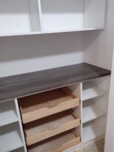 A white closet with open shelves, a dark wood countertop, and two wooden pull-out drawers partially open below the counter showcases stylish reach in closet concepts. Closet Concepts of Grand Rapids