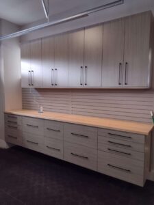 A wall-mounted cabinet set with upper and lower storage units, wood countertop, and slatwall backing adds stylish closet storage to any modern office or workspace. Closet Concepts of Grand Rapids