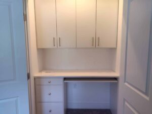 Small built-in desk area with white cabinets above, drawers on the left, and an open space beneath the countertop—perfect for organizing with closet systems—set between two doors. Closet Concepts of Grand Rapids