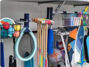 A garage wall with organized sports equipment, including balls, racquets, croquet mallets, bats, and scooters stored in baskets and hanging on hooks—showcasing smart closet systems beyond the traditional walk in closet. Closet Concepts of Grand Rapids