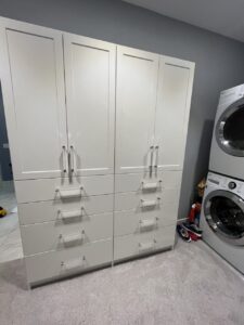 A white storage cabinet with eight drawers and four doors stands next to a stacked washer and dryer, offering closet concepts perfect for keeping your laundry room organized. Closet Concepts of Grand Rapids