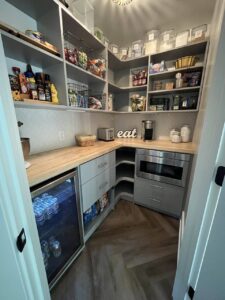A modern pantry with gray shelves, countertop appliances, organized food containers, snacks, a mini fridge with drinks, and a decorative "eat" sign on the counter—perfect for showcasing your closet storage or pantry organization concepts. Closet Concepts of Grand Rapids
