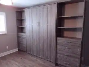A built-in wooden wall unit with a central cabinet, inspired by closet concepts, flanked by open shelves and drawers on both sides, in a room with wood flooring. Closet Concepts of Grand Rapids