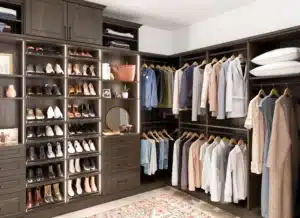 A neatly organized walk-in closet featuring innovative closet concepts with shelves of shoes, hanging clothes sorted by type and color, drawers, bags, pillows, and a vanity mirror on a countertop. Closet Concepts of Grand Rapids